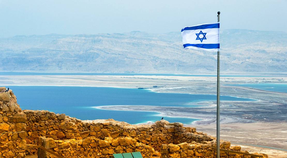 israeli-flag-with-the-ruins-on-masada-with-the-dead-sea-on-the-background-889843646_5113x3409